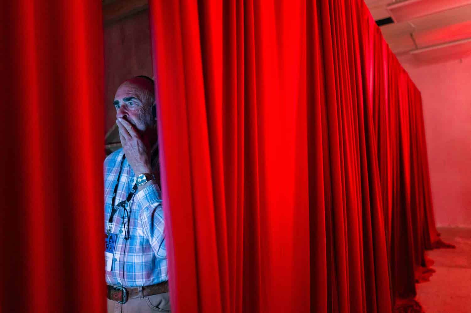 A visitor looking out from between the red curtains of a viewing booth