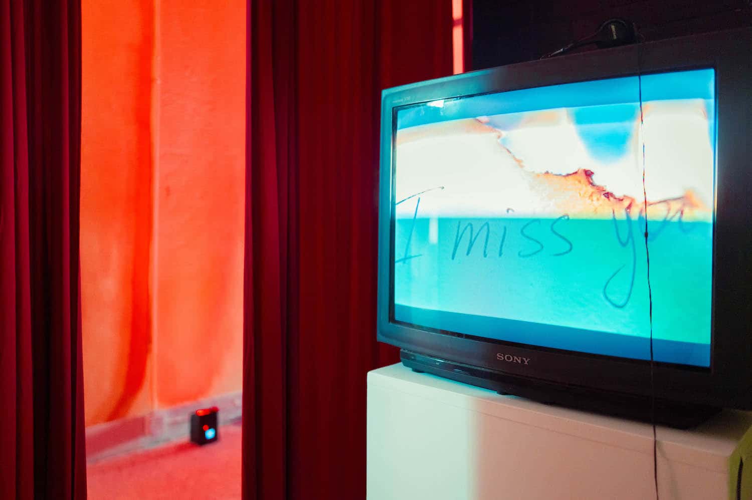 Inside a booth: a film playing on a CRT television beside the red curtain
